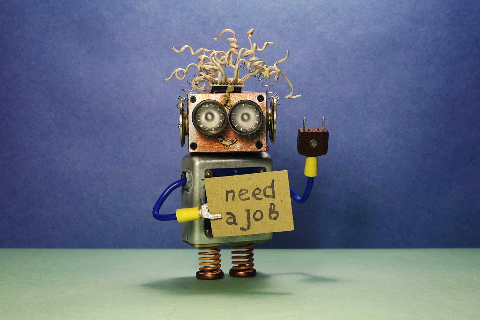 robot looking for a job. the crazy unemployed toy robot holds cardboard announcement handwritten text need a job. blue green background.