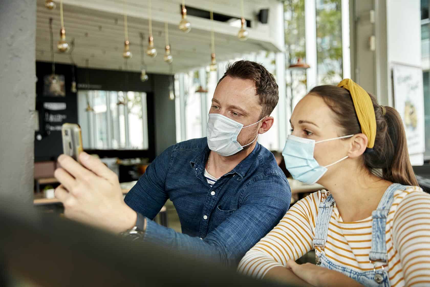 cafe,united kingdom,two people wearing face masks, using a smart phone, waving during a face time call.