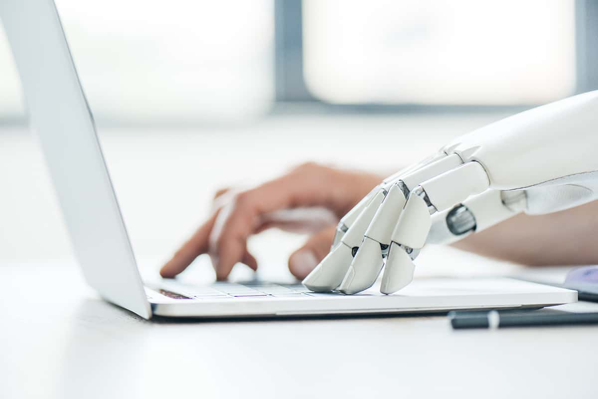 selective focus of human and robot hands typing on laptop at wor