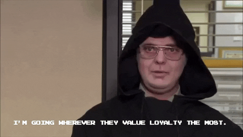 Dwight Shrute wearing glasses and a black hooded cloak sits indoors and says, "I'M GOING WHEREVER THEY VALUE LOYALTY THE MOST." in white text at the bottom of the image.