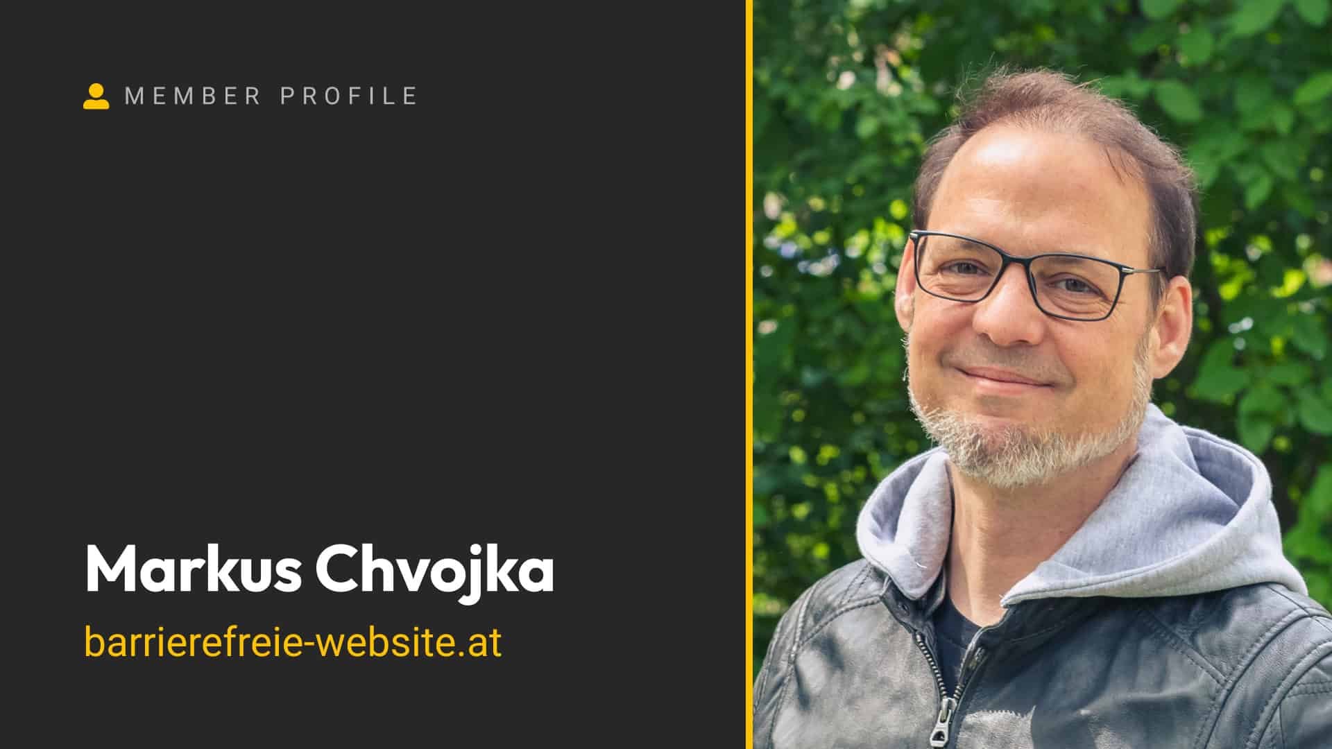 A smiling man with glasses and a gray hoodie outdoors.