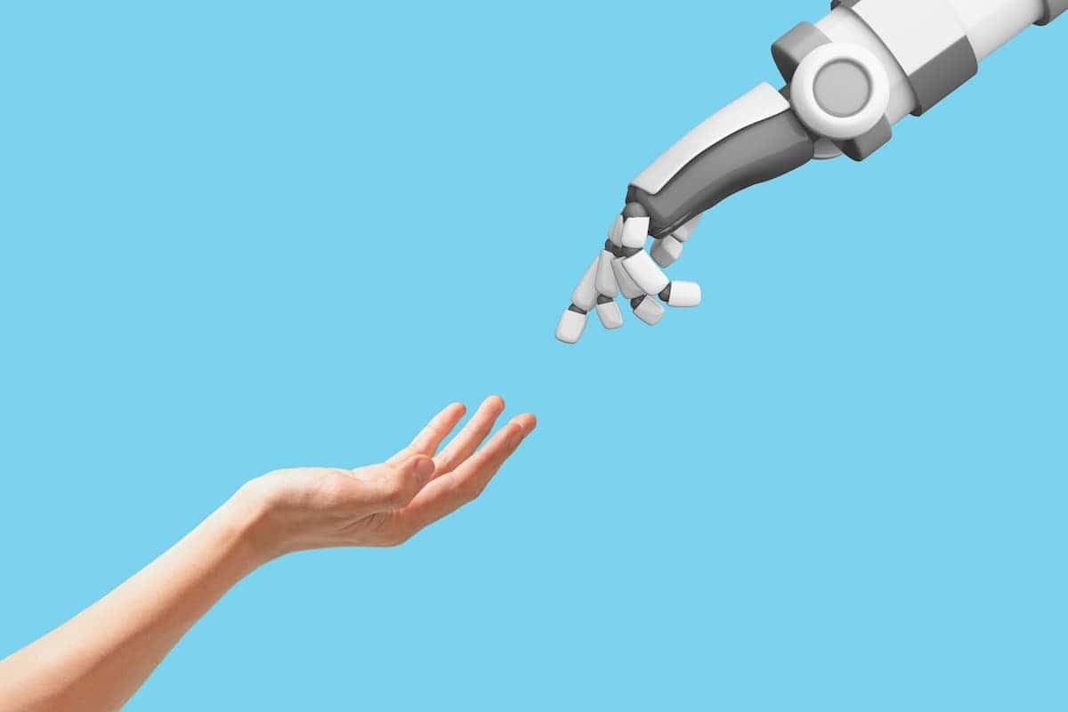 Human hand reaching out to robotic hand against blue background.
